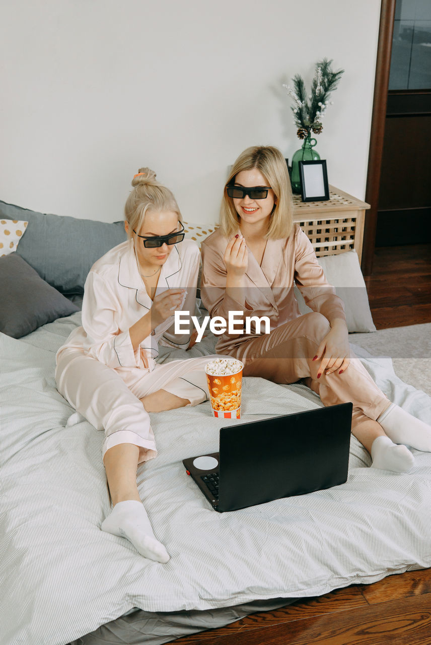 Blondes at home watch a movie on a laptop with 3d glasses and eat popcorn. concept of friendship.