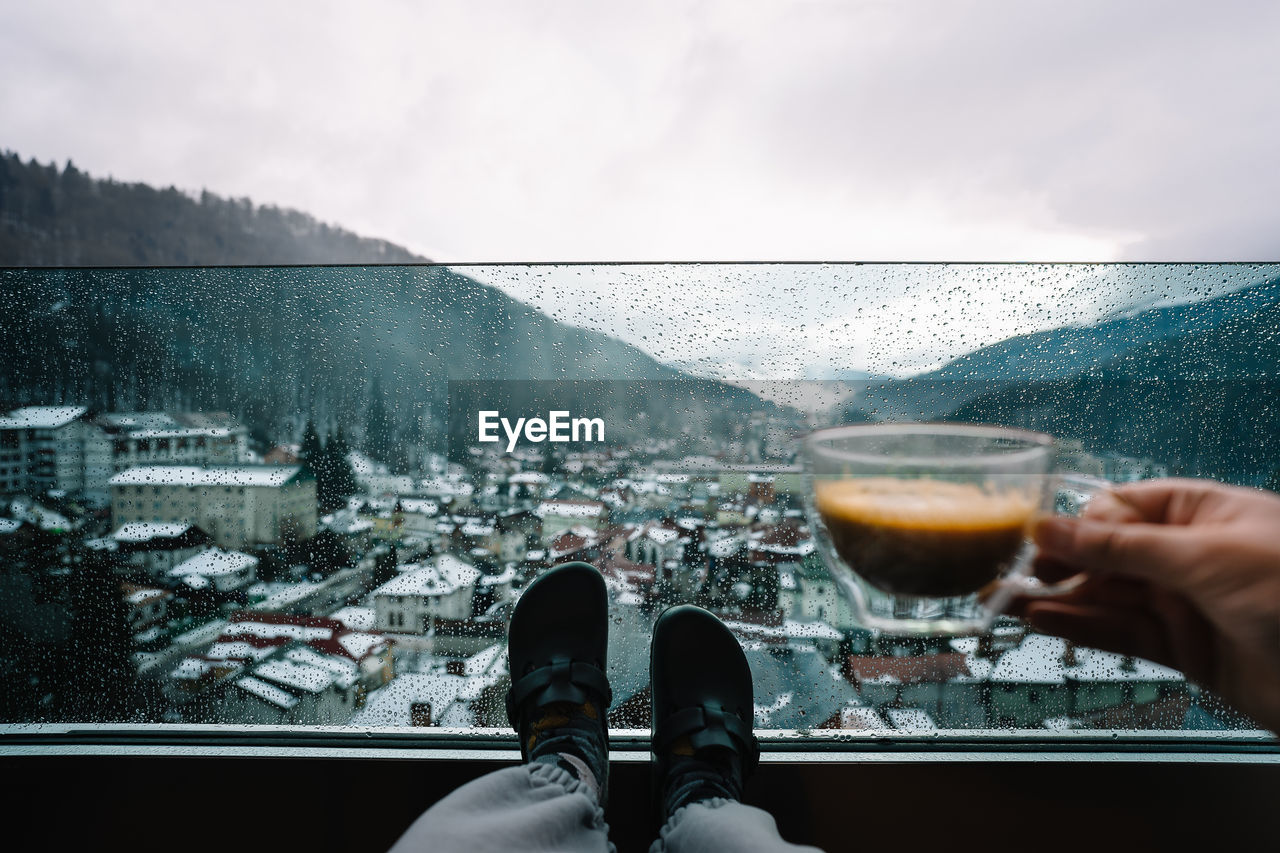 Low section of woman with drink in balcony at mountains against sky