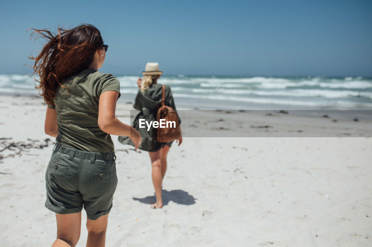 Rear view of female friends walking at beach on sunny day