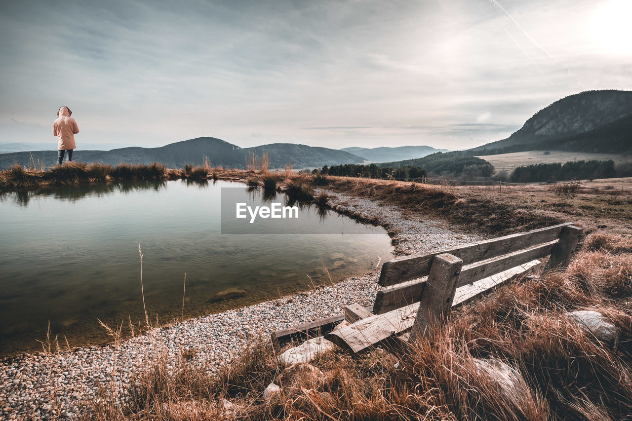 Rear view of man standing by lake against sky