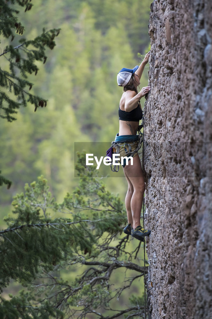 Side view of female hiker climbing rock in forest