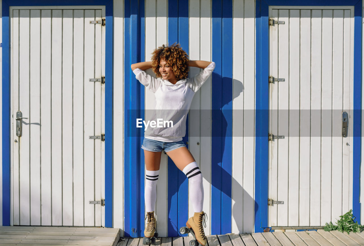 Full length of young woman with frizzy hair standing against building