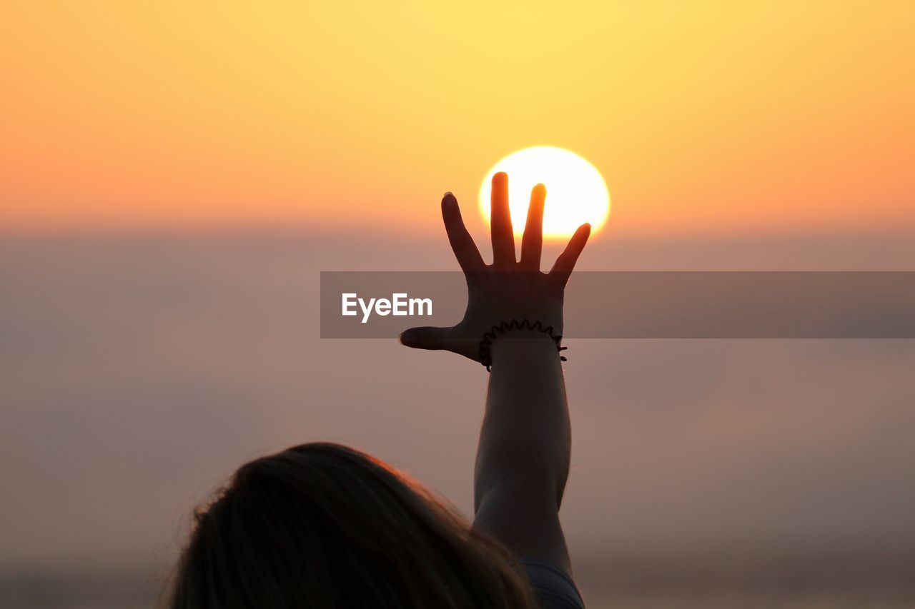 Optical illusion of woman touching sun during sunset