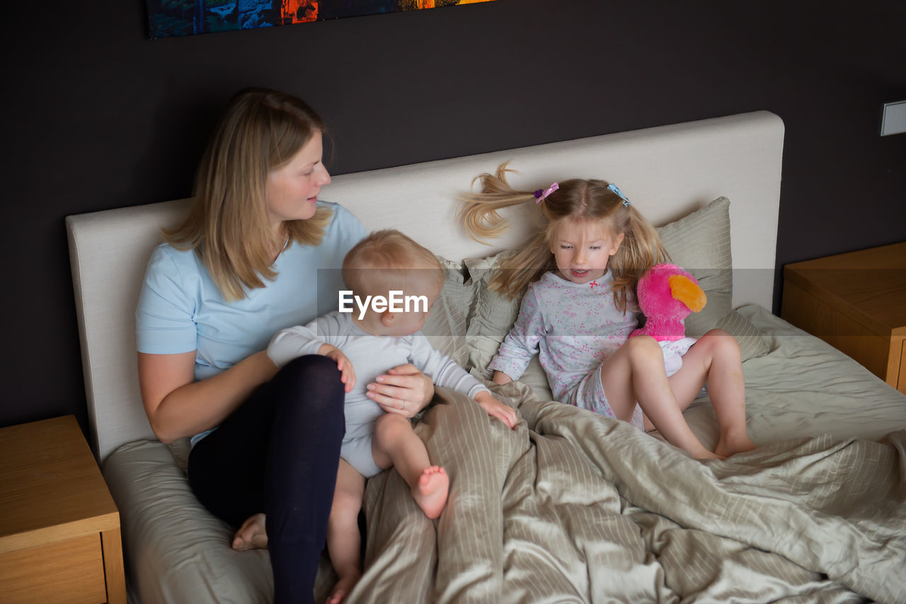 High angle view of mother with children sitting on bed at home