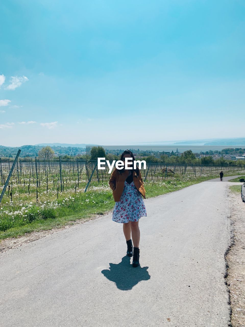 Full length of woman standing on road against blue sky