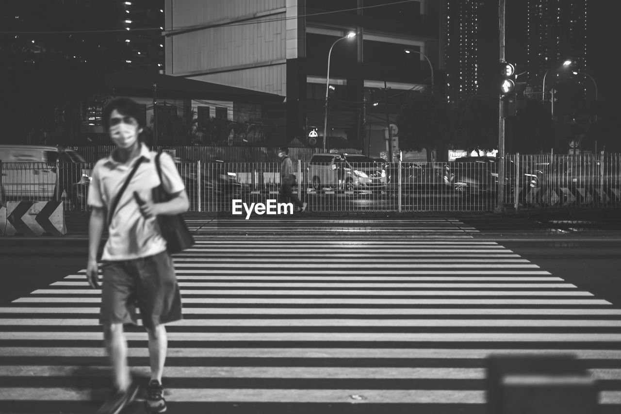 FULL LENGTH OF MAN CROSSING ILLUMINATED ROAD