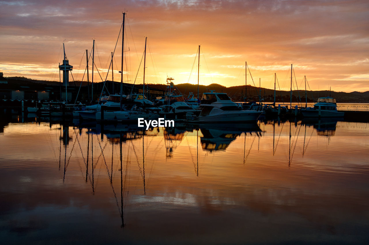 Sailboats moored at harbor against sky during sunset