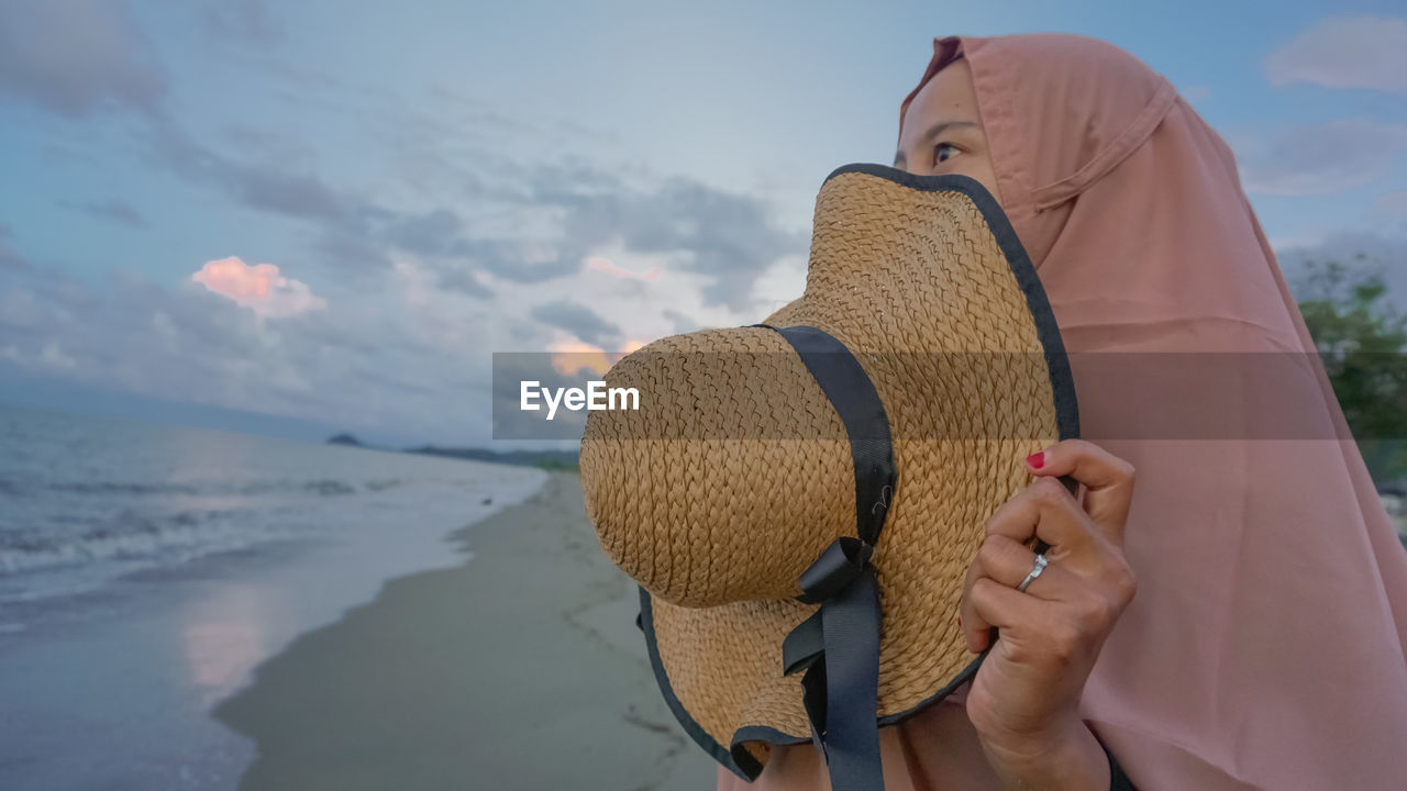 Midsection of woman holding hat against sky during winter