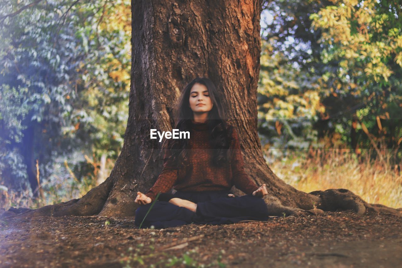 Full length of young woman practicing yoga against tree trunk in forest