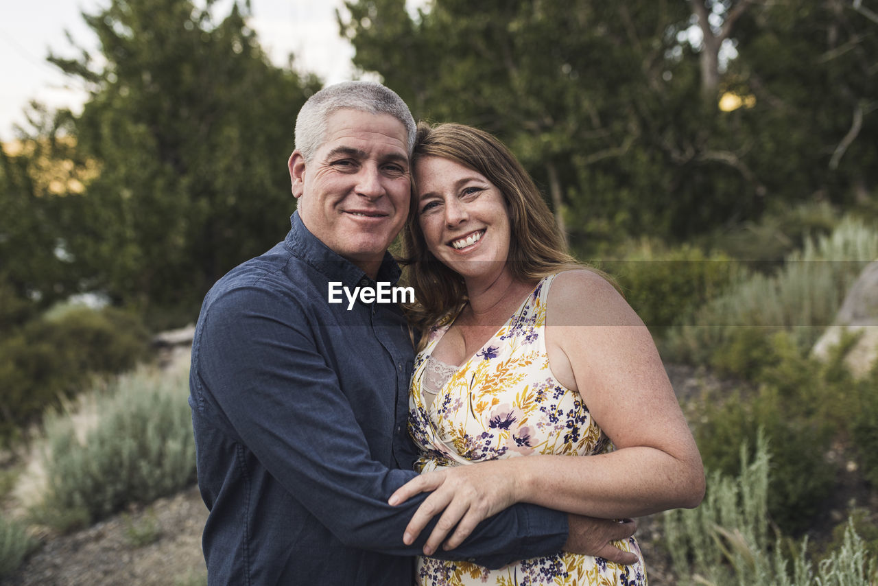 Portrait of happy couple embracing while standing against trees in forest