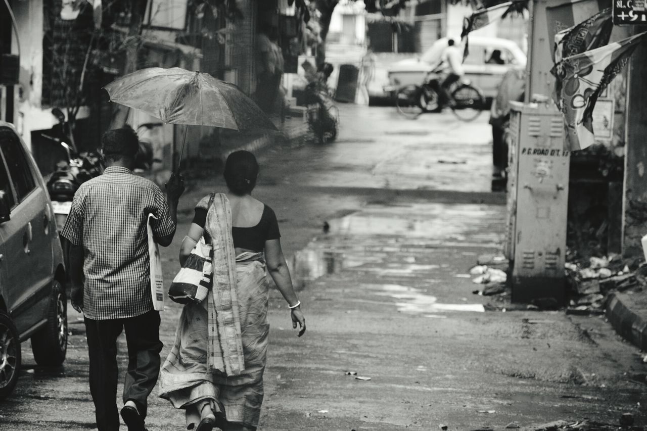 Rear view full length of man holding umbrella with woman on street