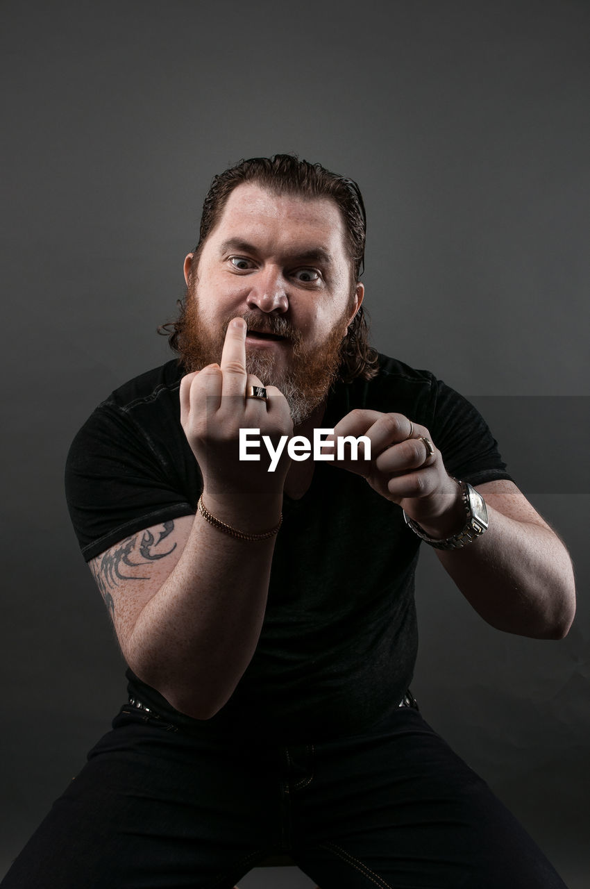 Mid adult man gesturing obscene gesture while sitting against black background