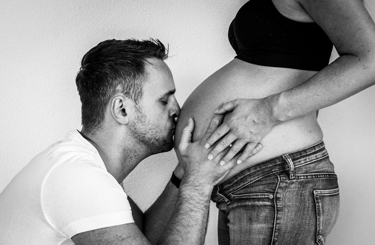 Man kissing on man pregnant woman abdomen against wall