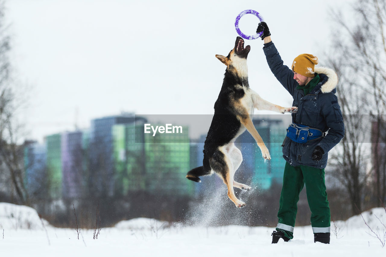 Man playing with dog in snow against sky