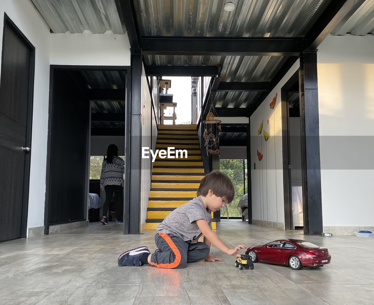 Side view of boy kid playing on the floor with car toy red color. house stairs behind 