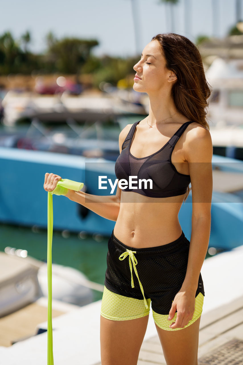 Young woman exercising with resistance band while standing on land