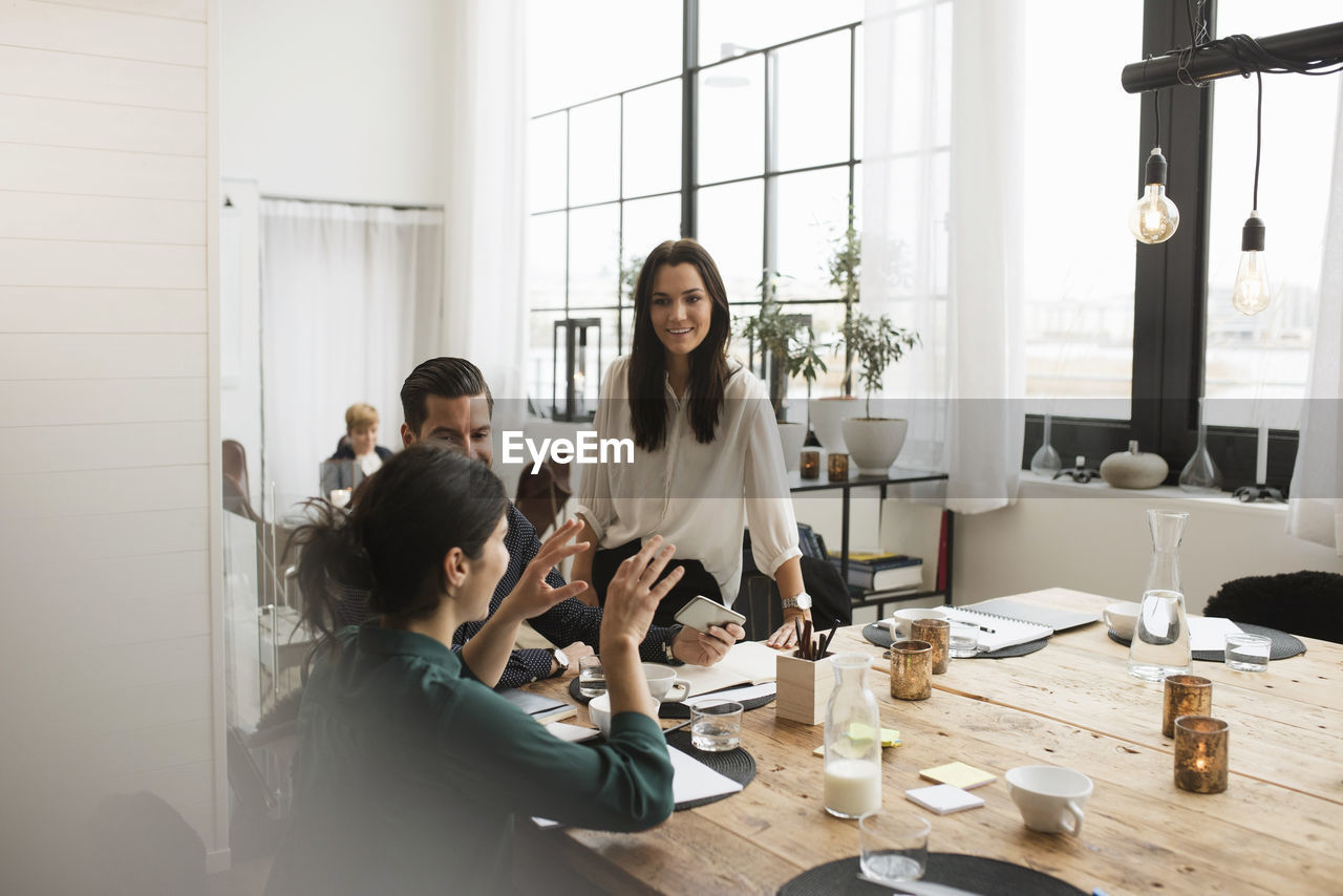 Smiling coworkers looking at businesswoman explaining during meeting in office