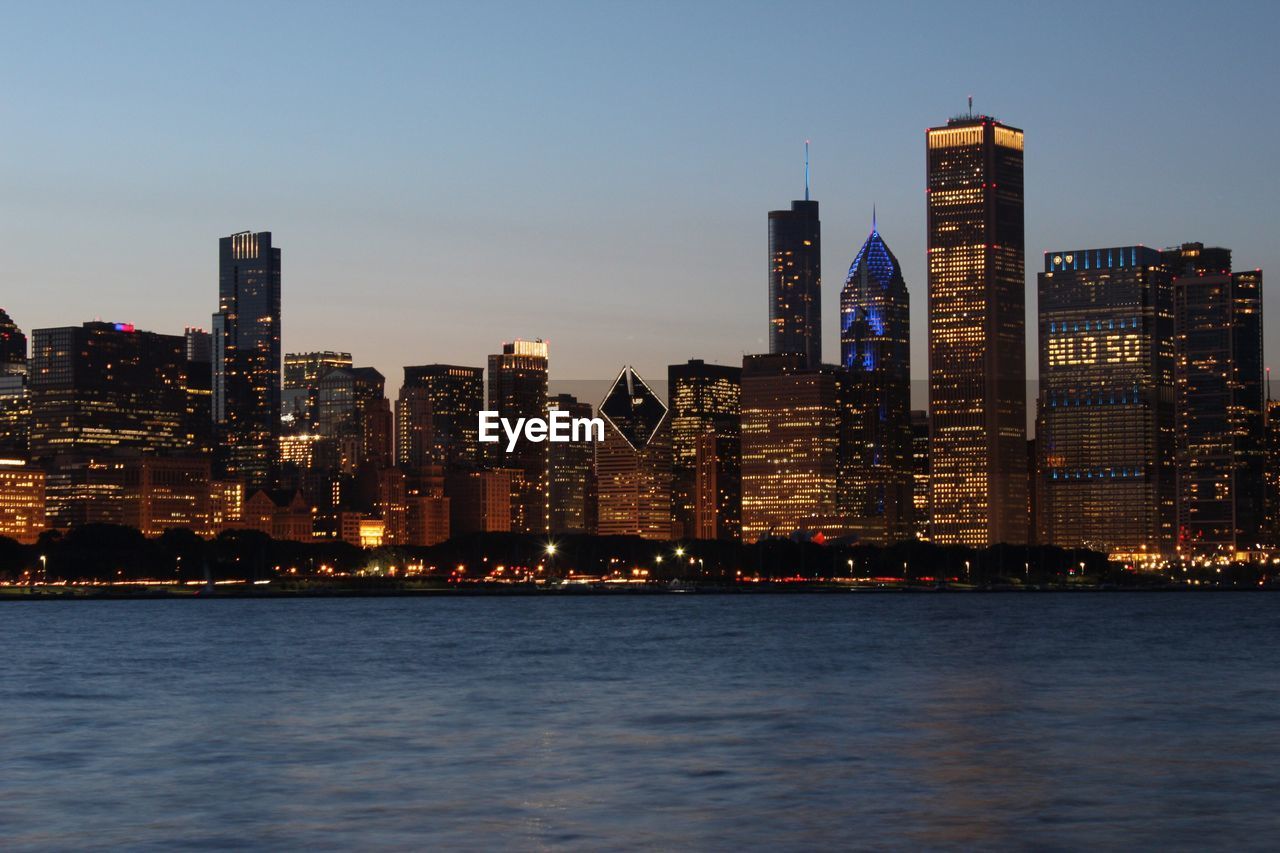 River by illuminated urban skyline against sky