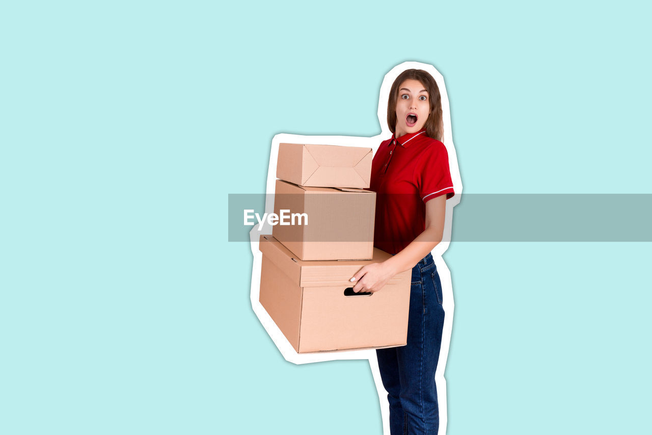 Portrait of shocked young woman holding box against blue background