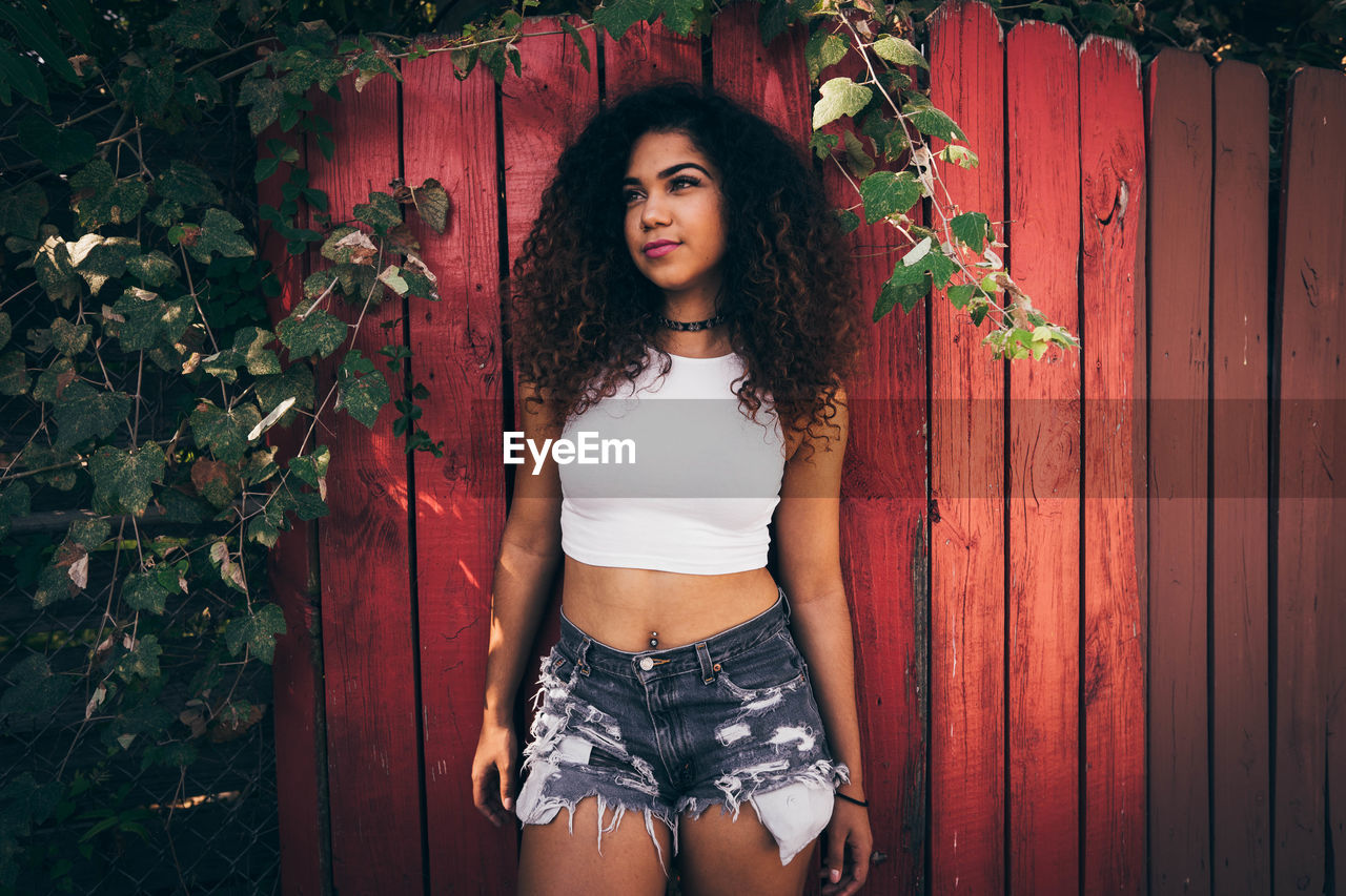 PORTRAIT OF YOUNG WOMAN STANDING AGAINST PLANTS