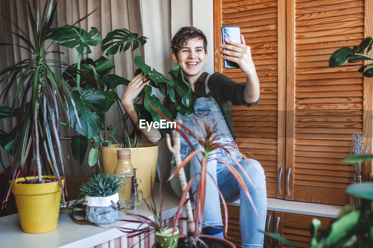 Girl makes photo with smartphone for social media, home plants on balcony, green room, gardening