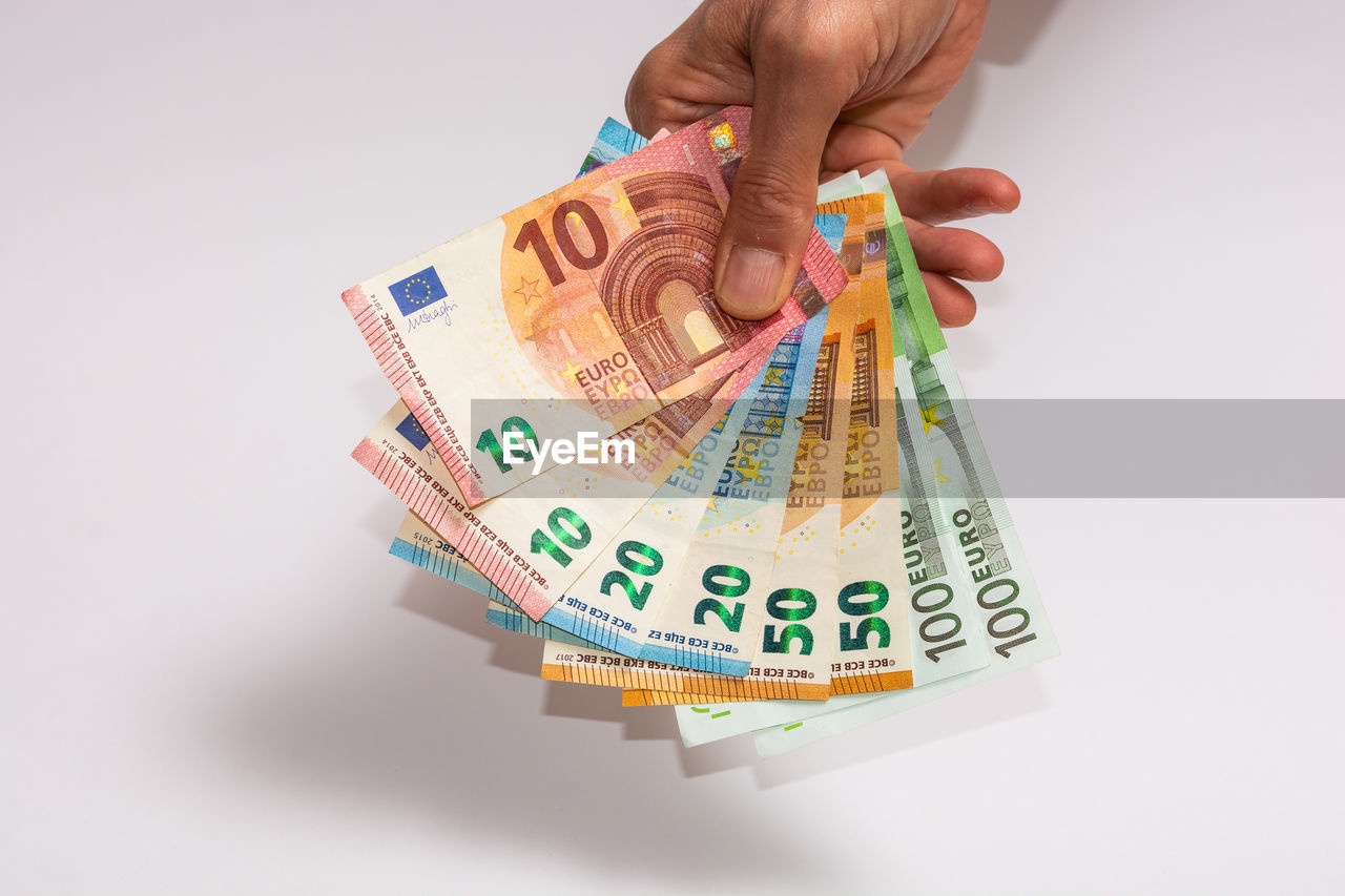 Cropped hand holding paper currency against white background