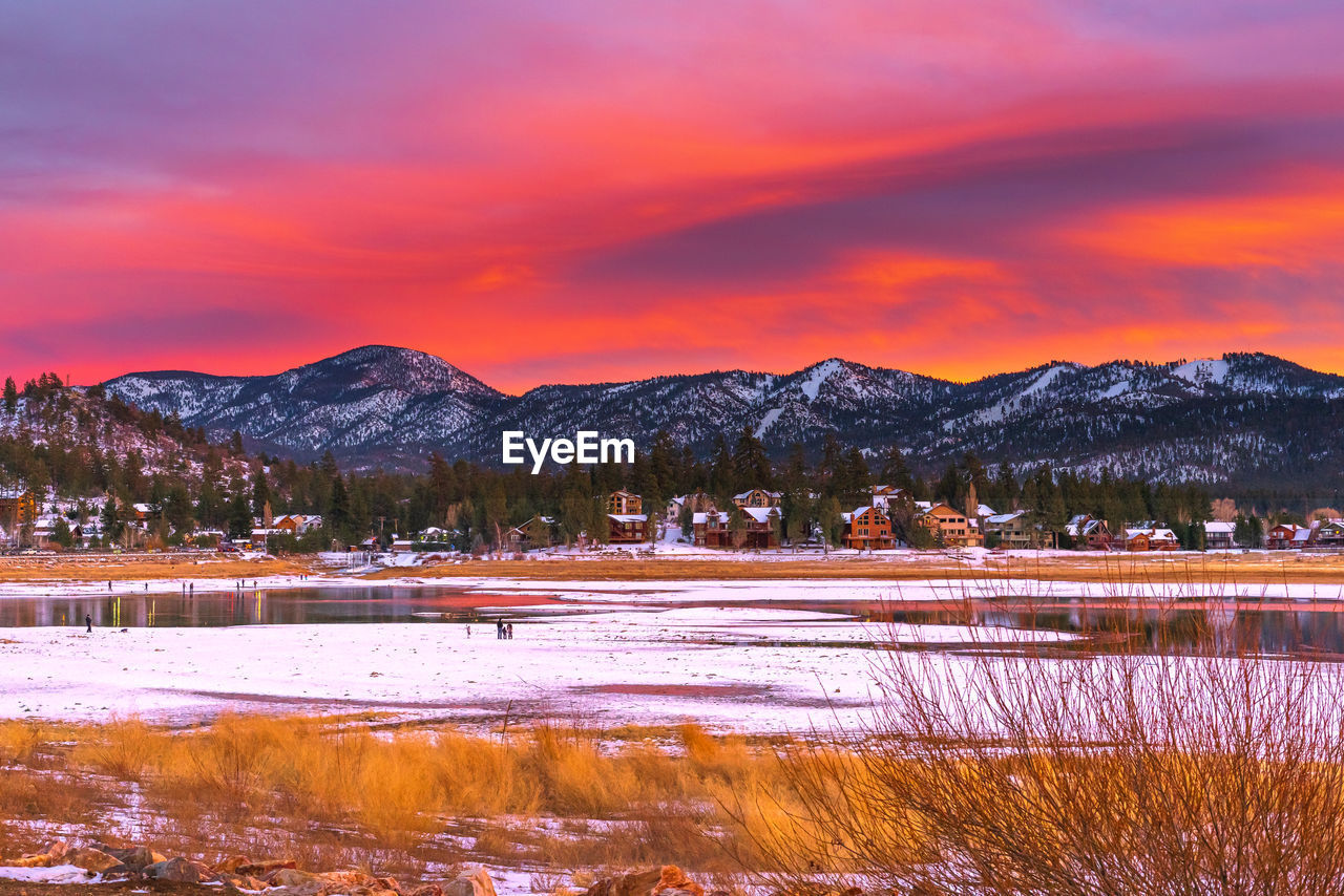 Scenic view of lake by snowcapped mountains against orange sky