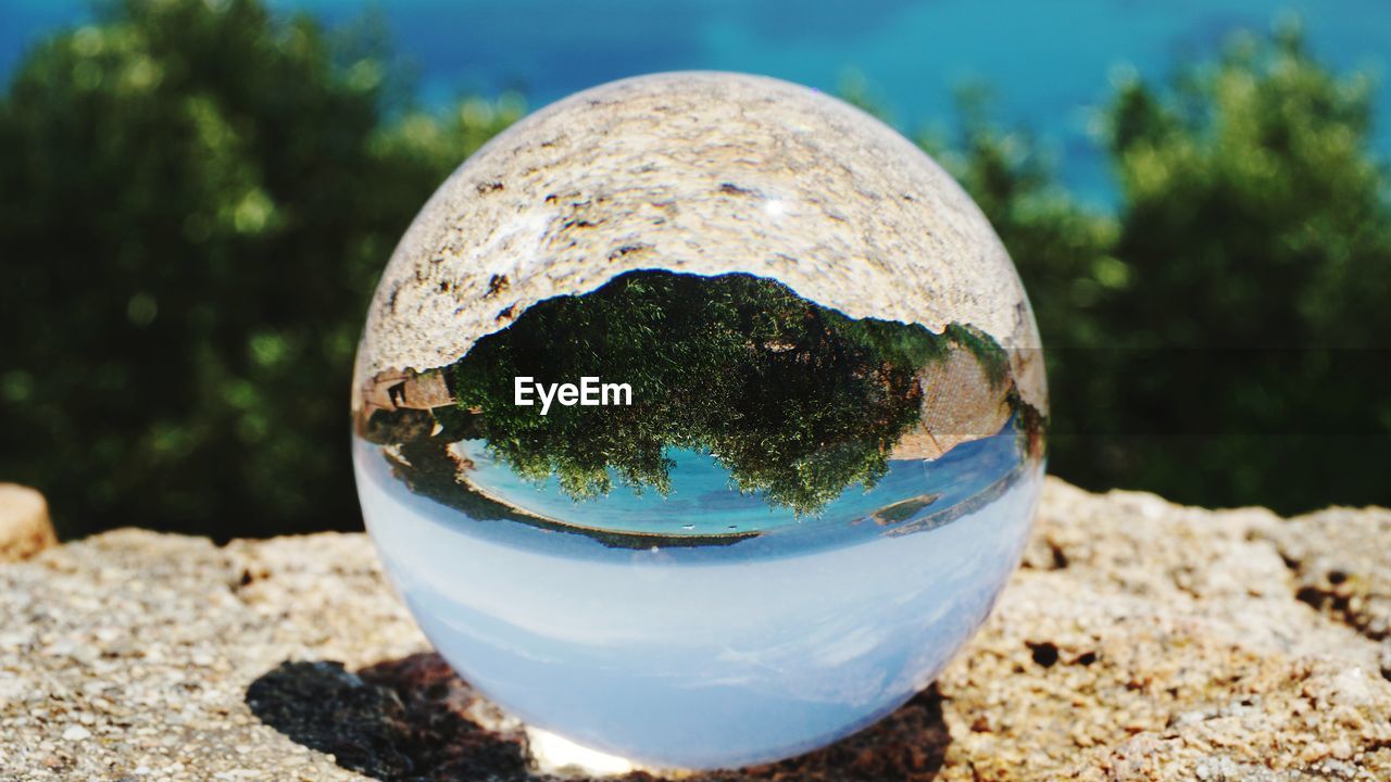 CLOSE-UP OF CRYSTAL BALL WITH REFLECTION OF TREES IN WATER