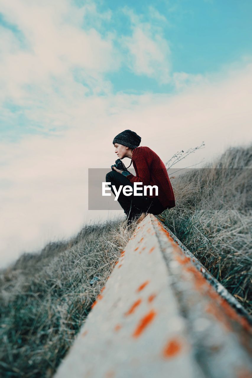 Woman sitting on field against sky