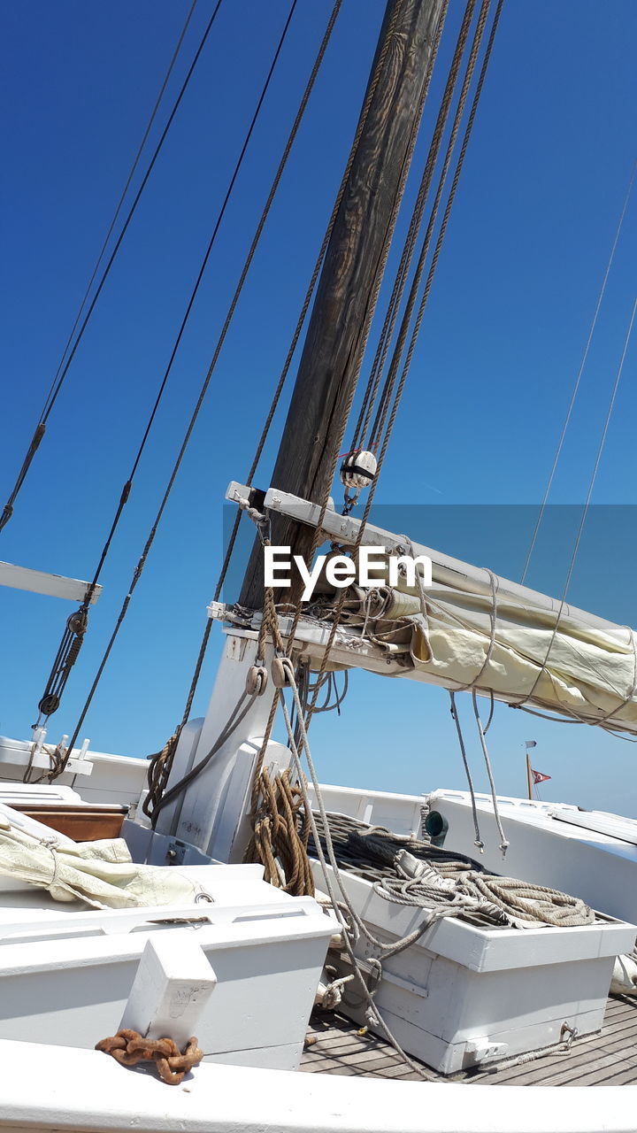 Low angle view of sailboats moored at harbor against clear blue sky