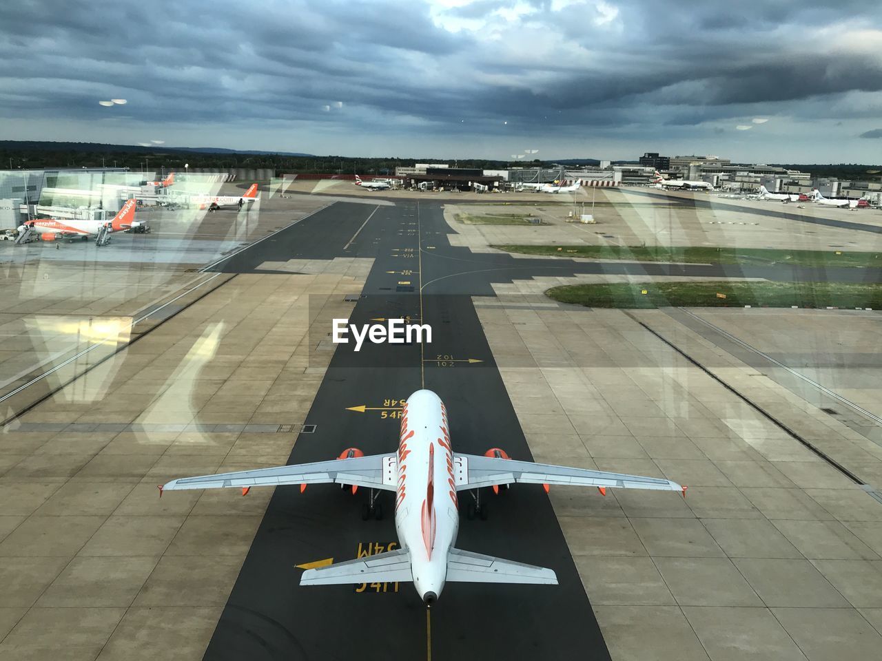 HIGH ANGLE VIEW OF AIRPLANE FLYING OVER AIRPORT RUNWAY AGAINST SKY