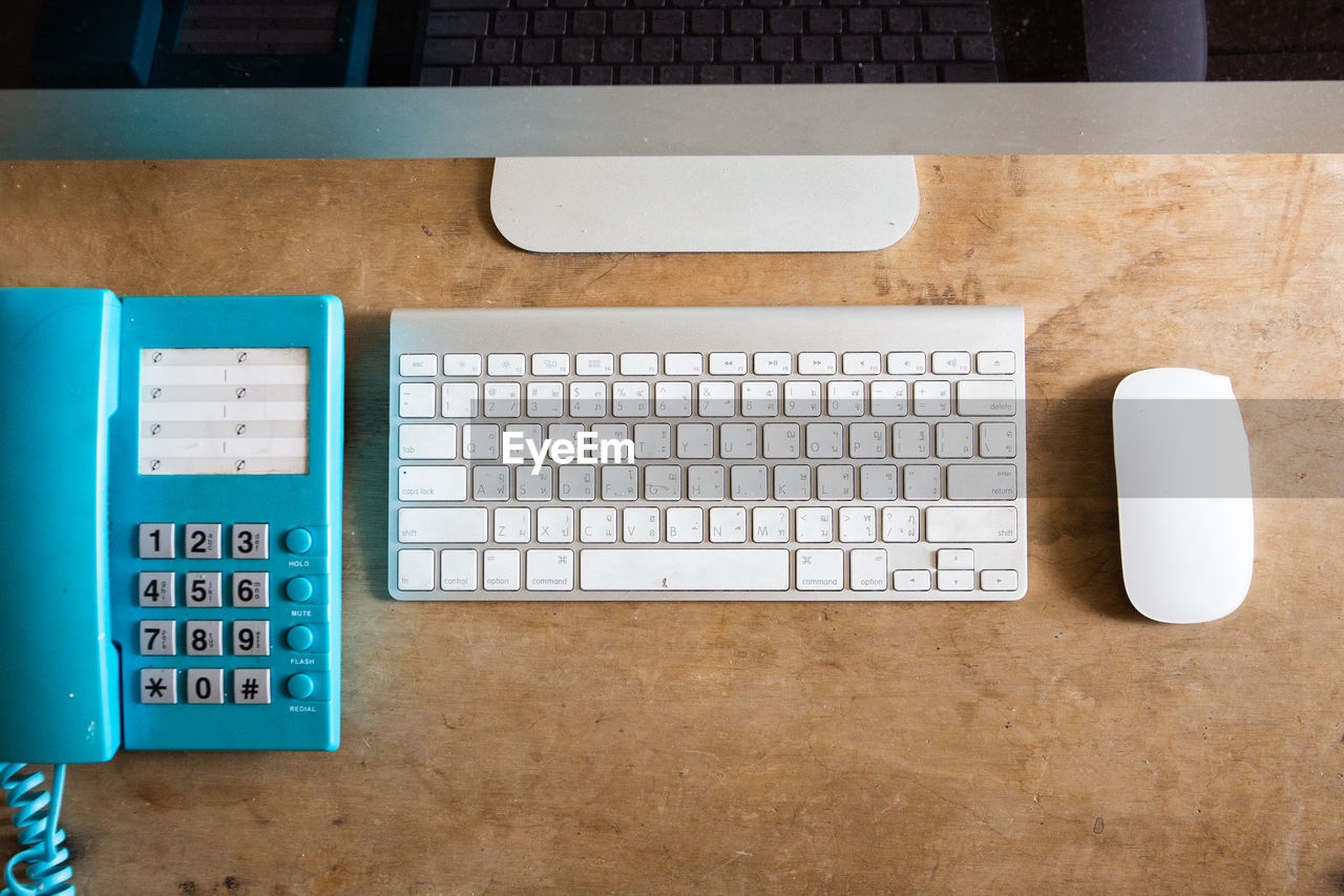 Directly above shot of keyboard by computer mouse and telephone on wooden table