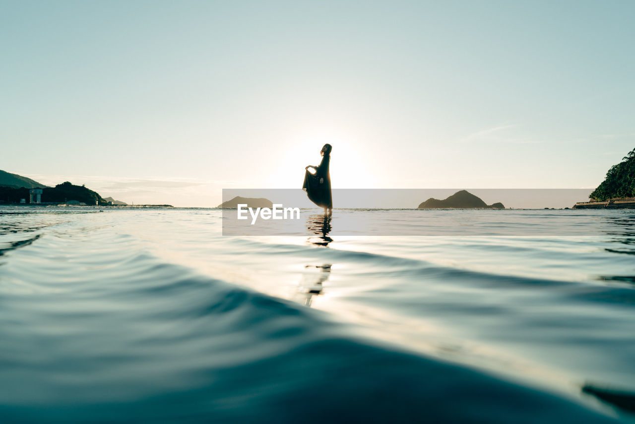 Silhouette woman standing in sea against sky during sunset