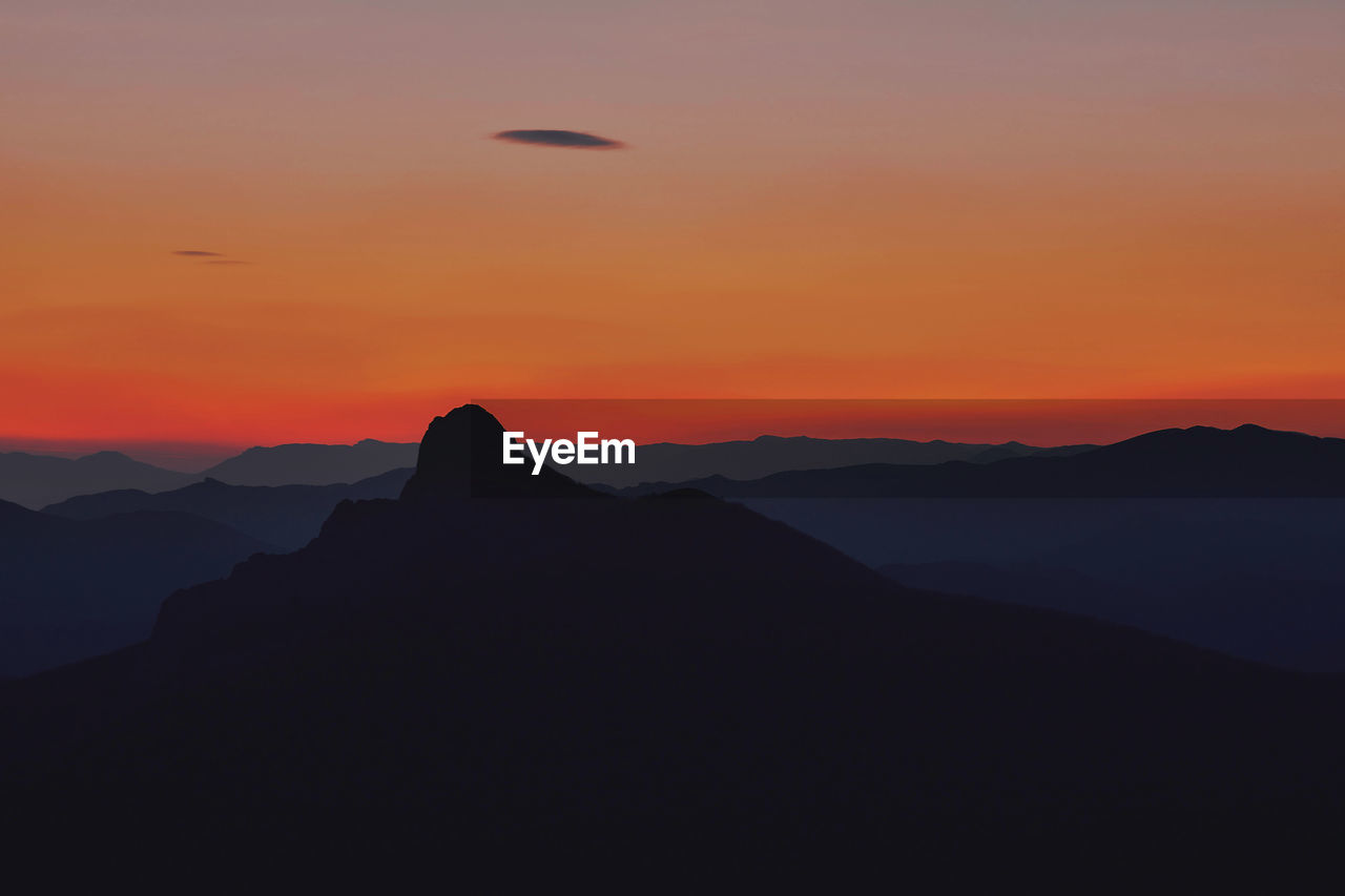 SILHOUETTE OF MOUNTAIN AGAINST ORANGE SKY