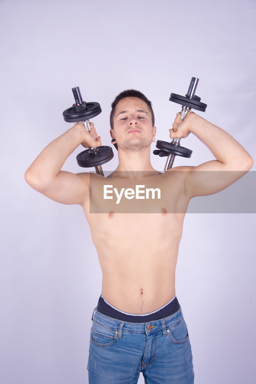 Shirtless man lifting dumbbells against purple background