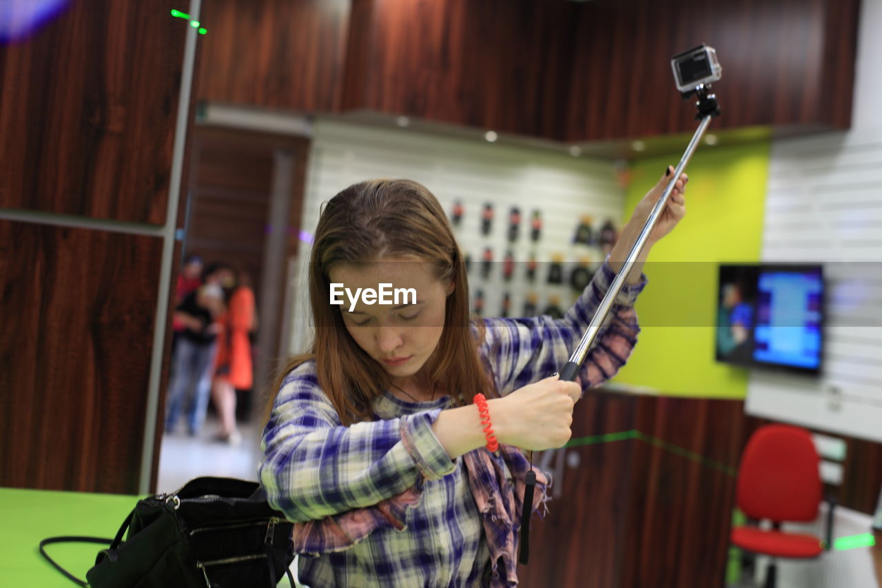 GIRL HOLDING CAMERA WHILE STANDING IN SHOP
