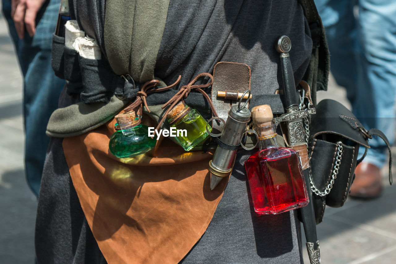 Midsection of man with perfume bottles and dagger standing outdoors