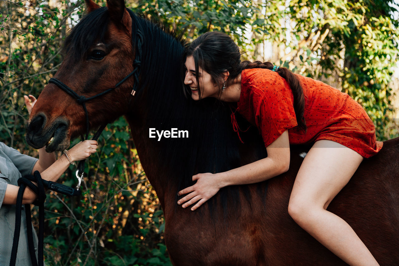 Young woman sitting on horse talking with friend in forest