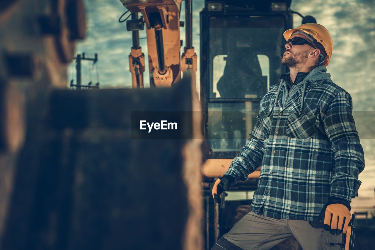 Man wearing sunglasses standing by earth mover at construction site