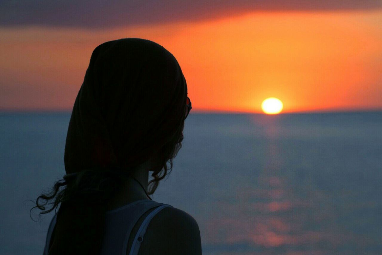 Close-up of woman overlooking calm sea at sunset