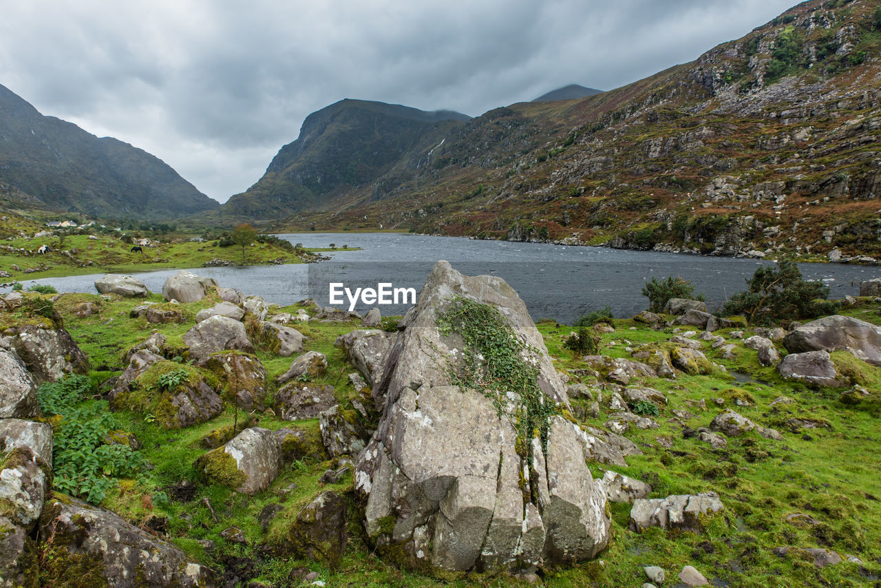 Scenic view of lake and rocky mountains against cloudy sky