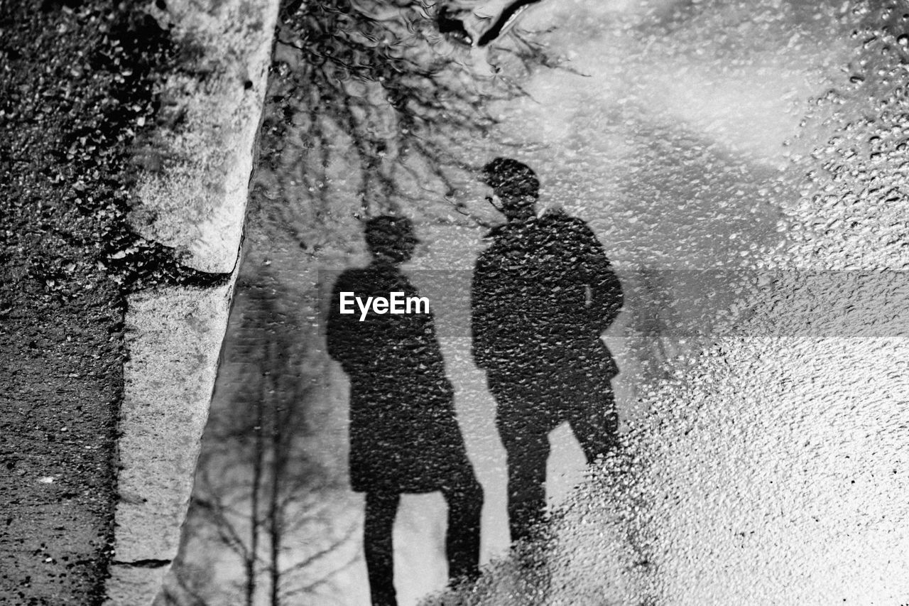 Friends reflecting in puddle on footpath