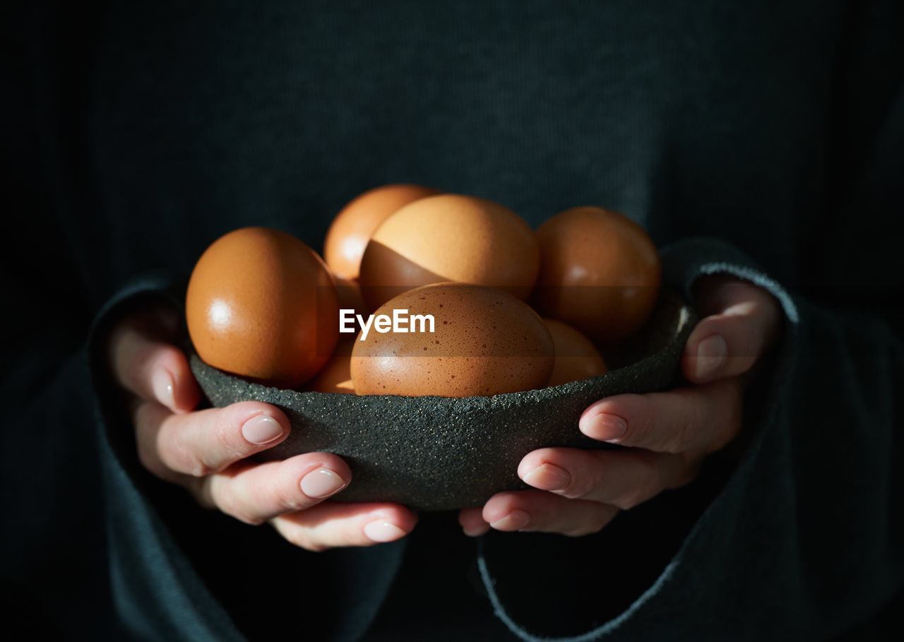 Unusual easter on dark background. bowl of brown eggs with hands. darkness, rays of sunlight