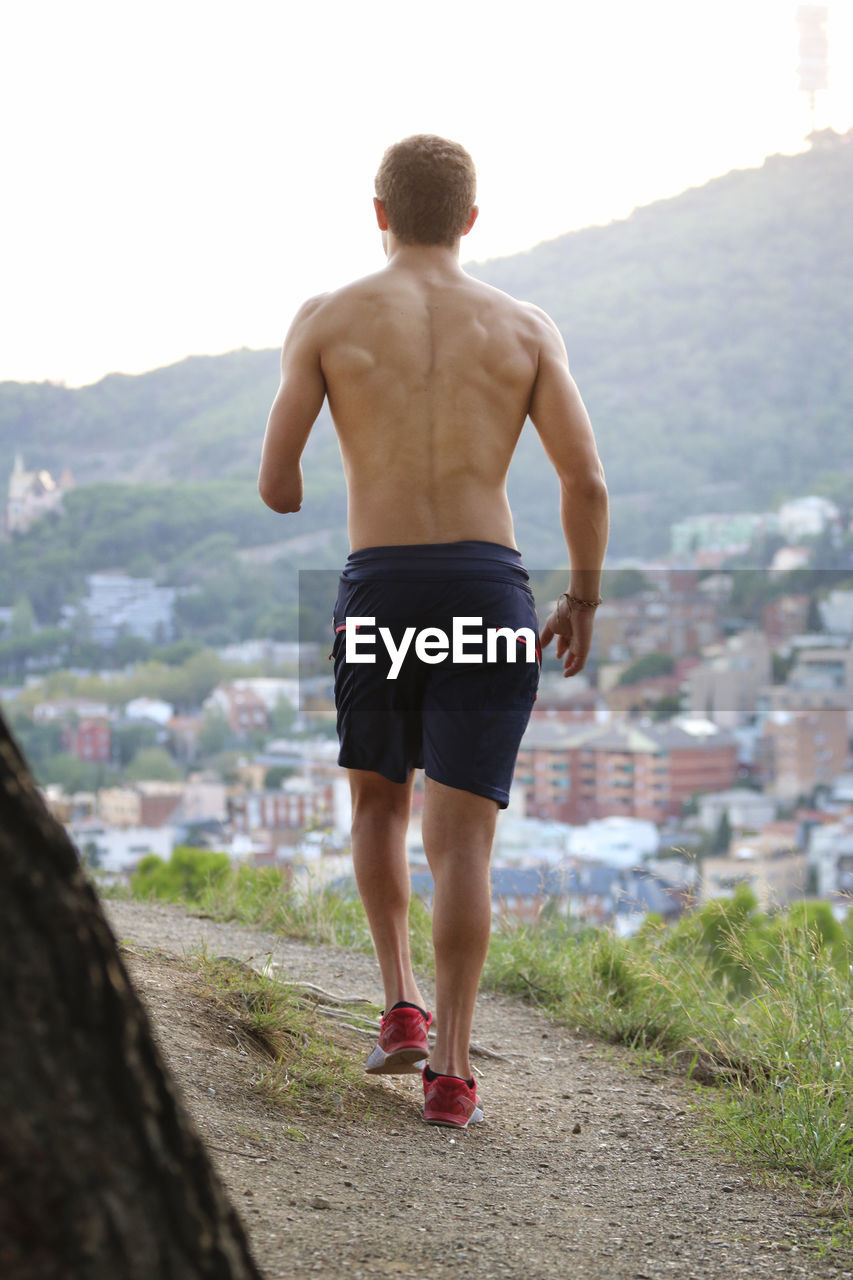 Rear view of physically challenged shirtless man jogging against cityscape