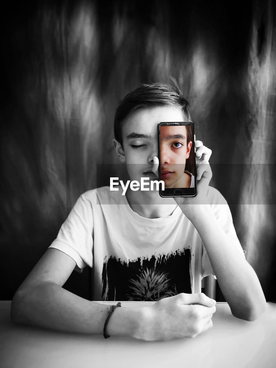 Teenage boy with eyes closed holding mobile phone while sitting at table