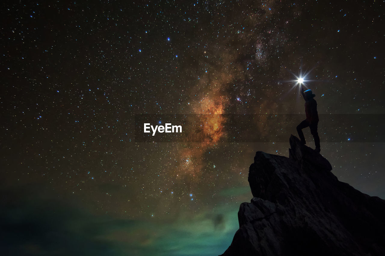 MAN STANDING ON ROCK AGAINST SKY AT NIGHT