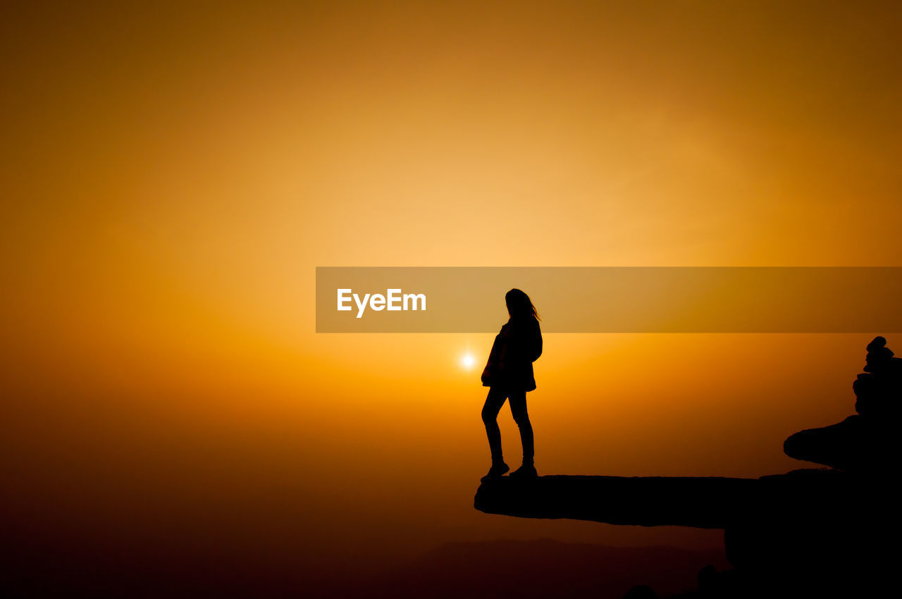 Silhouette woman standing on cliff against sky during sunset