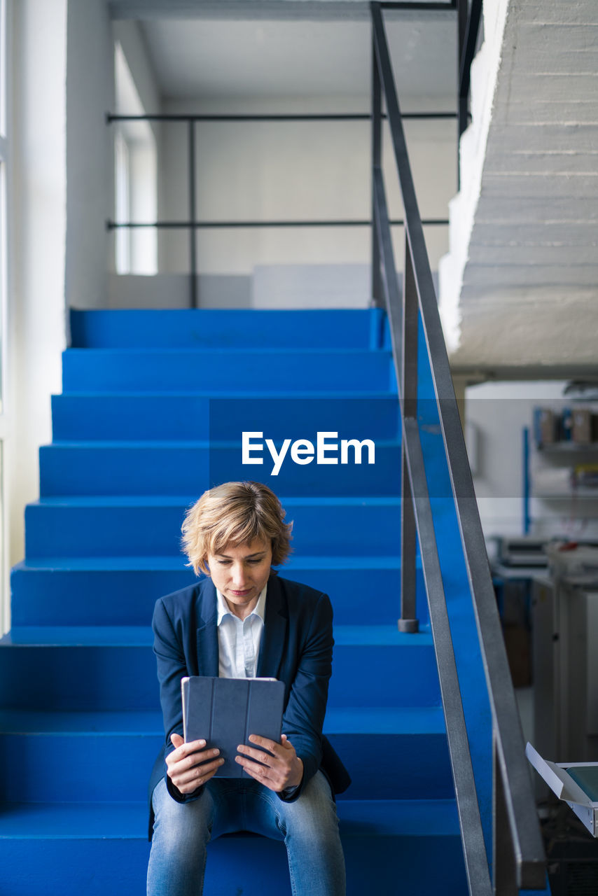 Female entrepreneur using digital tablet while sitting on steps in factory