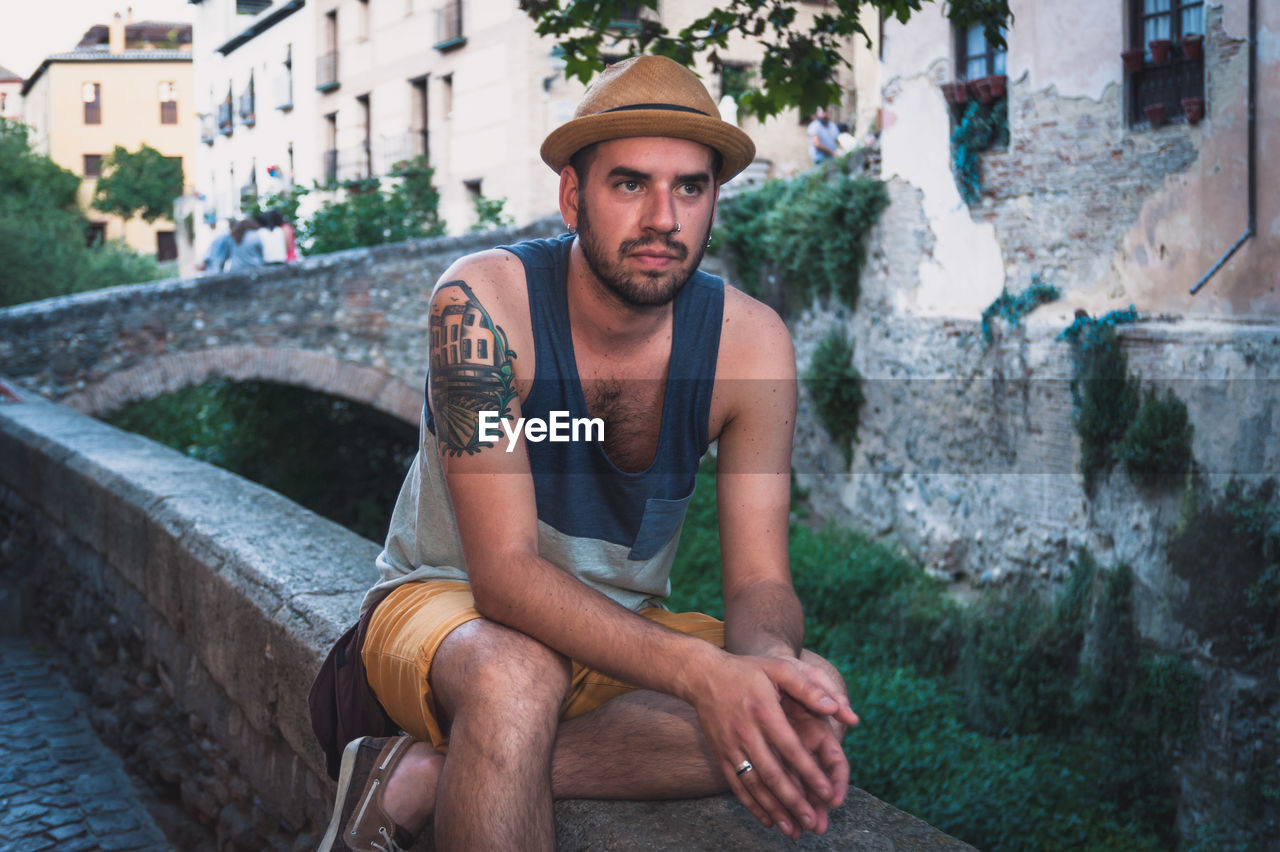 Man with hat sitting on retaining wall in town