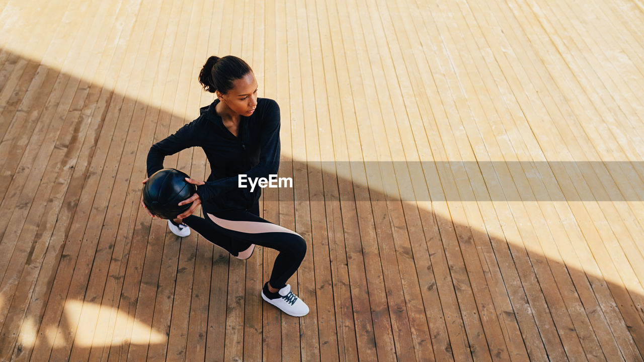 Full length of woman exercising with ball on boardwalk during sunny day